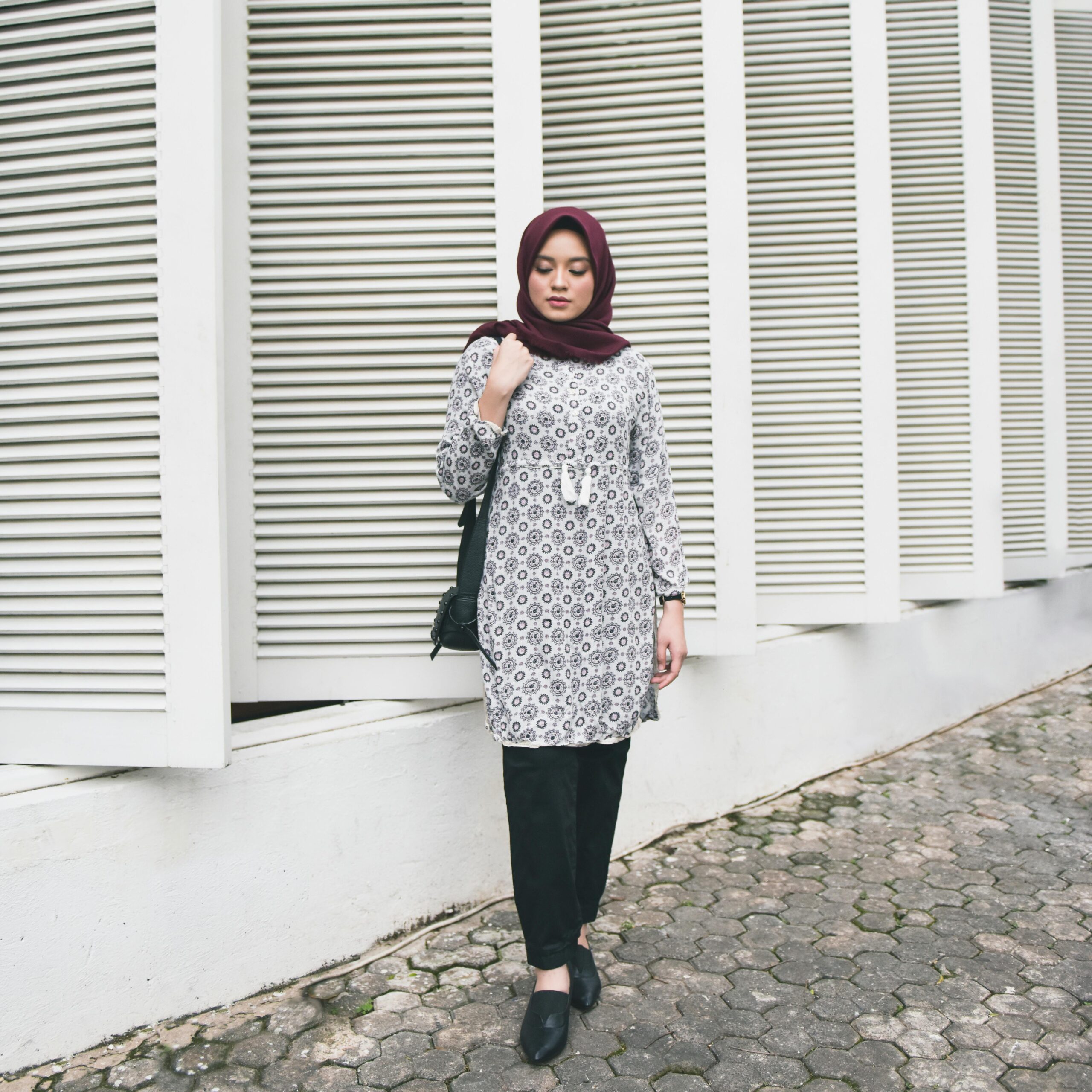 Fashionable woman in a patterned hijab posing against modern architecture outdoors.