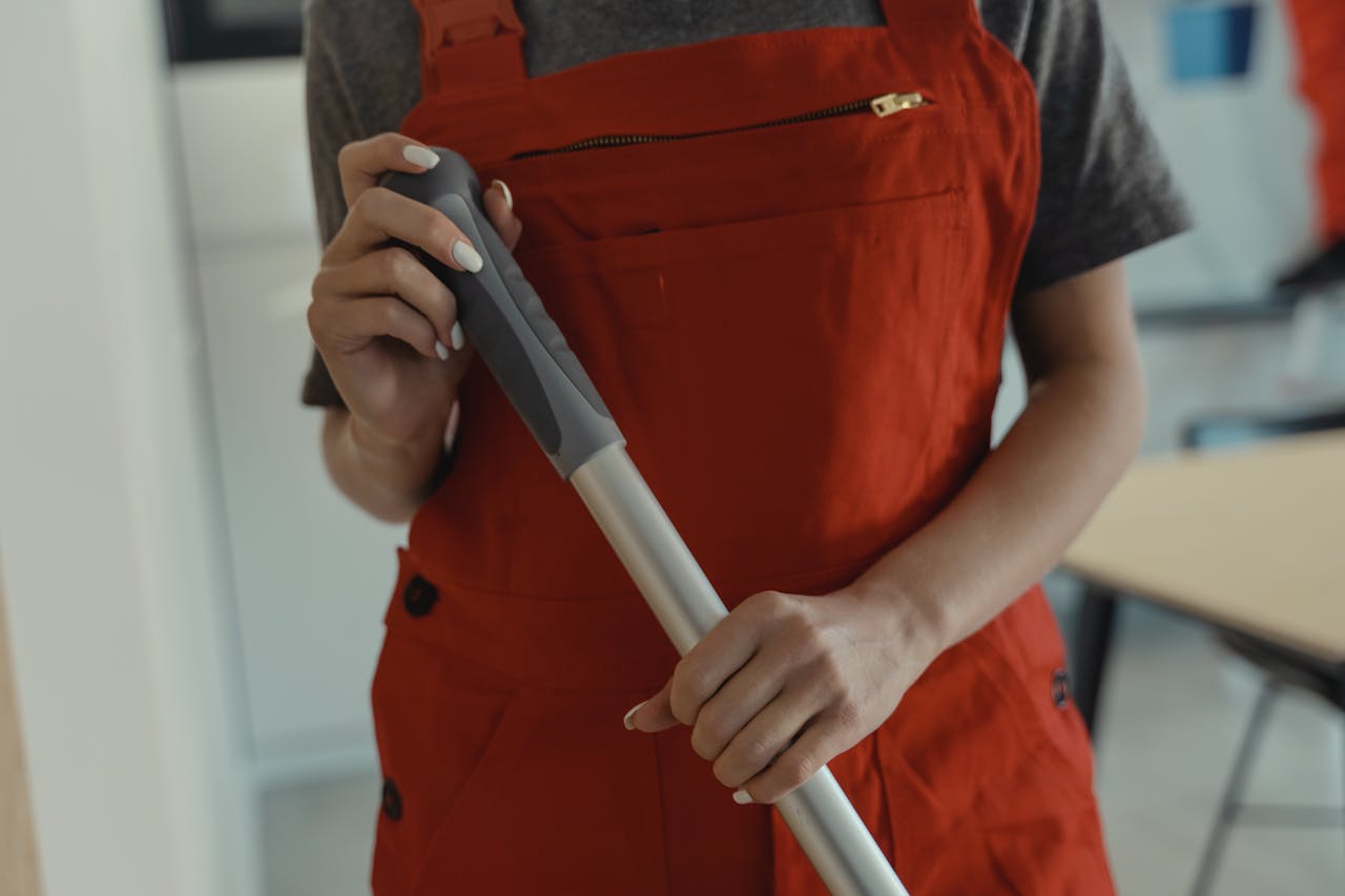 5 Important Things to Know Before Hiring a Maid in Singapore (Updated 2025) A woman in a red apron holding a mop handle, performing cleaning indoors.