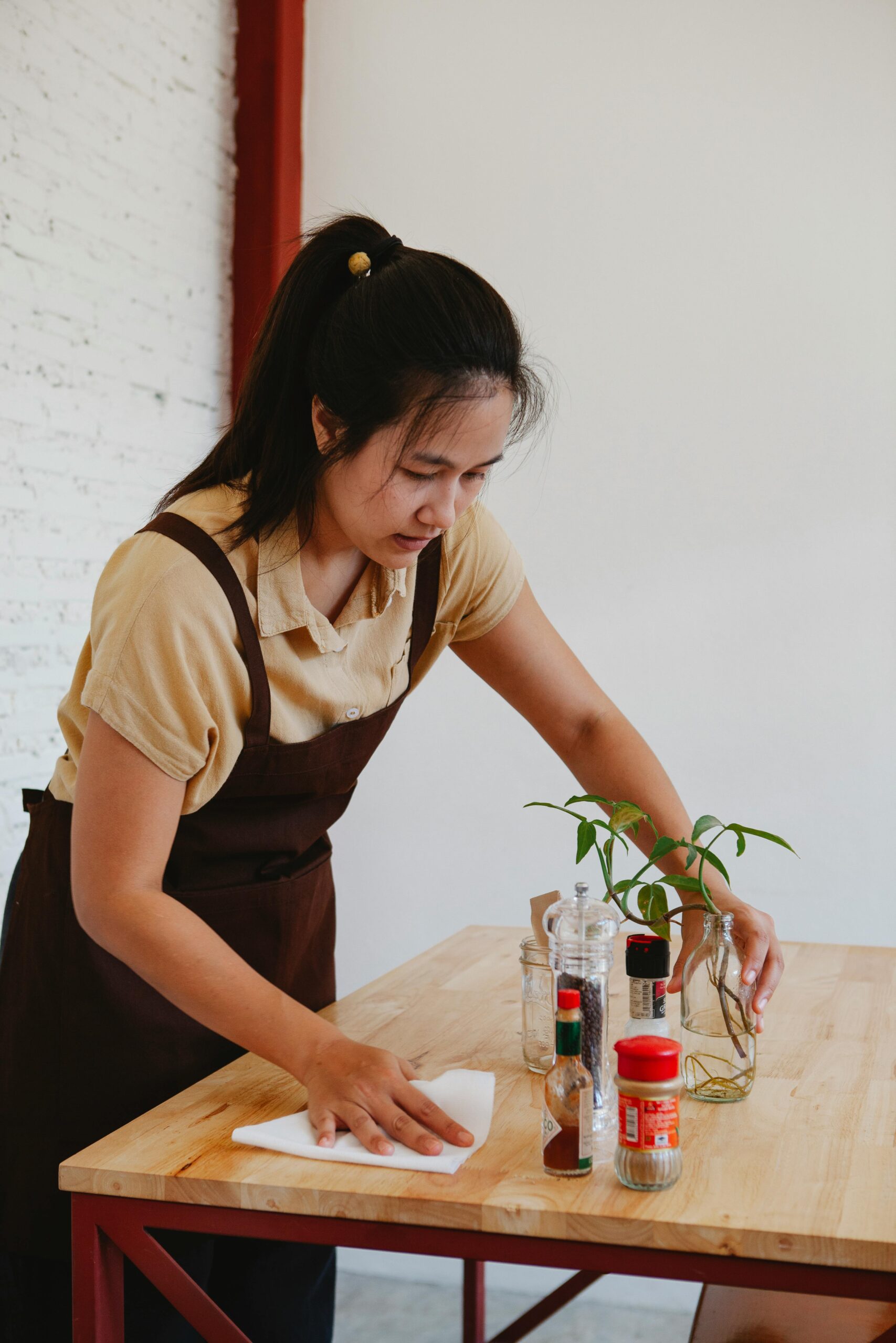 Asian woman cleaning a wooden table with a cloth in a cozy indoor cafe setting.