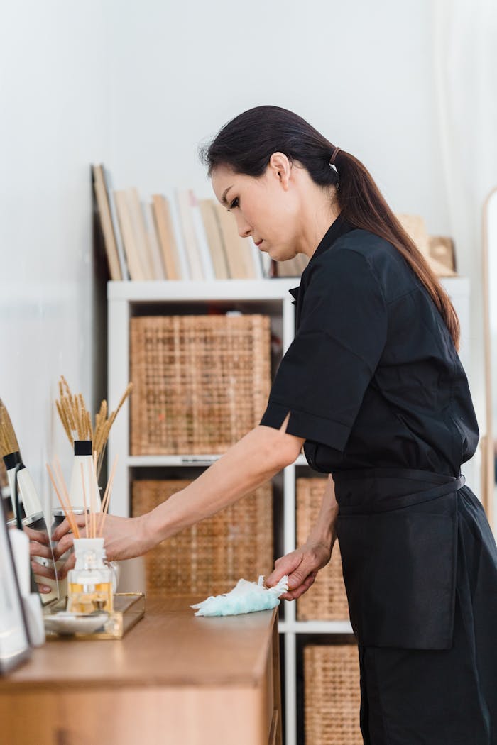 Industry Insight: How Singapore’s Maid Employment Landscape is Changing in 2025 Woman in black uniform cleaning a wooden counter indoors with shelves in the background.