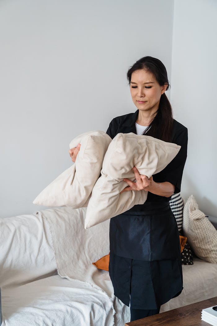 Your Maid’s First 30 Days: Tips for a Smooth Transition Into Your Home Smiling housekeeper arranging pillows on a sofa in a bright living room.